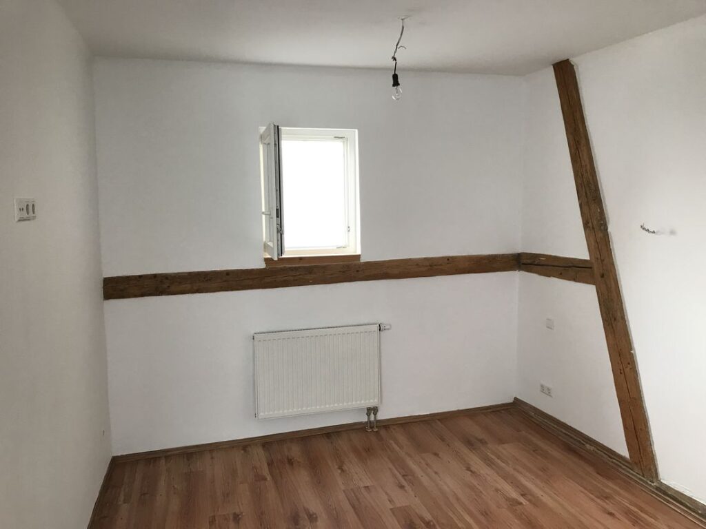 Leeres Zimmer mit Holzfußboden und Fenster.